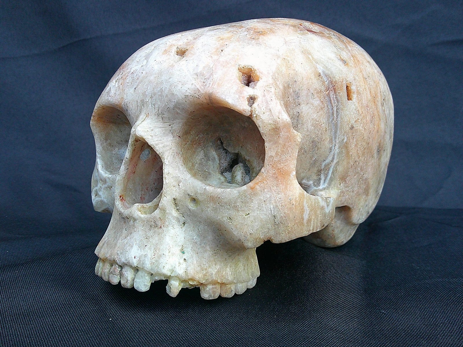 Perspective latérale de la sculpture “Le Caverneux”, crâne façonné dans une agate présentant des cavités et motifs naturels.