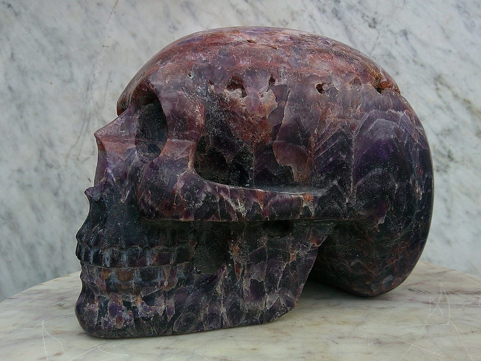 Perspective latérale de la sculpture “Vulcain d’Auvergne”, crâne façonné dans une améthyste d’Auvergne aux reflets clairs et sombres.