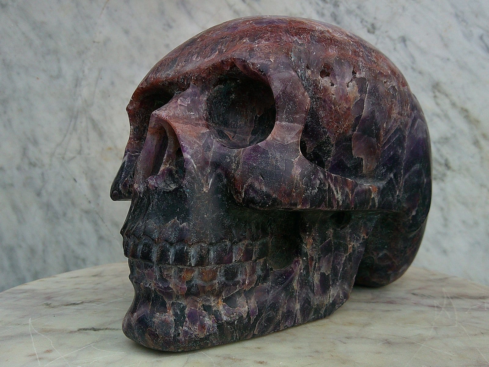 Crâne “Vulcain d’Auvergne” sculpté dans une améthyste chevron aux violets profonds et nuances claires.