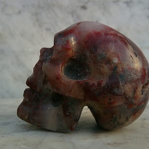 Profil gauche de la sculpture de crâne en agate rouge, blanche et grise – “Le Breton” – œuvre artisanale sculptée en Aveyron.