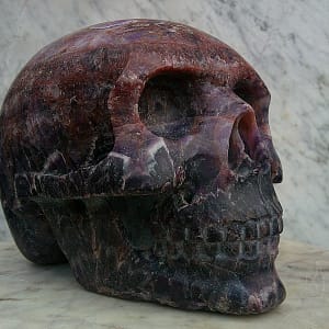 Sculpture “Vulcain d’Auvergne”, crâne en améthyste chevron montrant les bandes contrastées et les inclusions rougeâtres du minéral.