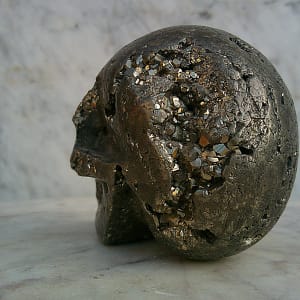 Crâne sculpté en pyrite, vue arrière, sculpture minérale en pierre naturelle cristallisée, pièce d’art présentée en galerie.