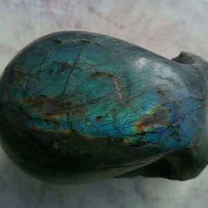 Vue de dessus d’un crâne sculpté à la main en labradorite polie, mettant en valeur la labradorescence bleue et verte sur la voûte crânienne. Sculpture minérale artisanale en labradorite.
