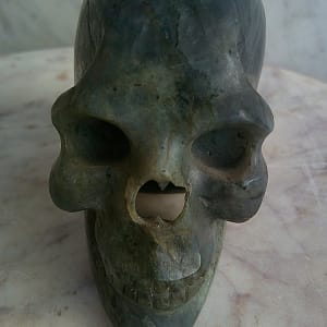 Vue frontale d’un crâne sculpté à la main en labradorite polie, révélant les volumes du front, les orbites profondes et la structure du visage. Sculpture minérale artisanale en labradorite.
