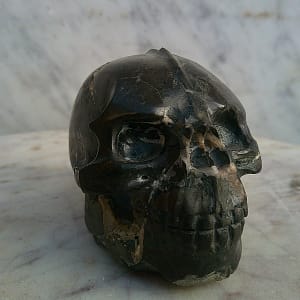Vue de face d’un petit crâne sculpté en pierre magnétique entièrement polie, mettant en évidence la crête centrale, les orbites profondes et la structure de la mâchoire. Sculpture minérale taillée à la main.