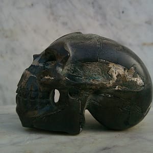 Vue latérale d’un crâne sculpté en pierre magnétique entièrement polie, petit format, mettant en valeur la ligne continue de la voûte crânienne et le travail de sculpture précis sur les volumes.