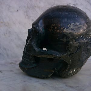 Sculpture de crâne humain en pyrite, vue arrière en trois-quarts, pièce unique sculptée à la main dans un bloc de minéral naturel, révélant la forme du crâne, les zones laissées plus brutes, les inclusions métalliques de la pyrite et les variations de texture issues du travail de sculpture à l’atelier.