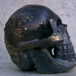 Sculpture de crâne humain en pyrite, vue de profil droit, pièce unique sculptée à la main dans un bloc de minéral naturel, mettant en valeur les inclusions métalliques de la pyrite, les variations de texture et le travail détaillé des volumes réalisé à l’atelier.