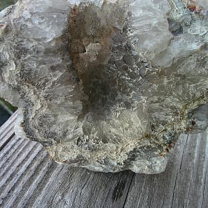 Crâne sculpté en agate naturelle, vue arrière de la géode, sculpture minérale montrant l’arrière brut et cristallisé de l’agate, structure géodique ouverte avec zones translucides et cristallisations naturelles visibles, travail artisanal de taille sur agate massive, pièce artistique en pierre dure exposée en galerie, sculpture de crâne en agate révélant la formation interne du minéral.