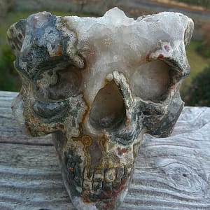 Crâne sculpté en agate naturelle, vue de face, pièce artistique en pierre dure présentant une géode d’agate aux bandes minérales visibles, sculpture minérale artisanale exposée en galerie, travail de taille sur agate massive, crâne décoratif en agate, art lapidaire et sculpture sur minéraux.