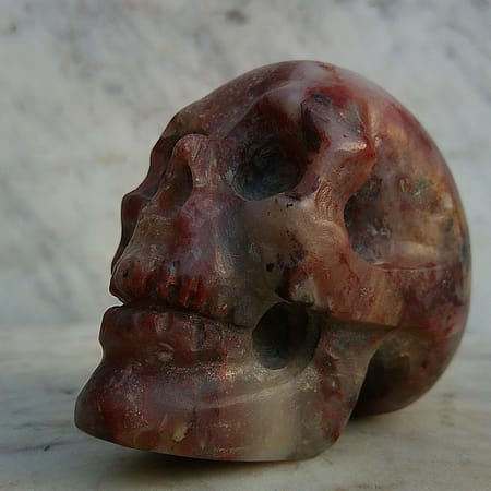 Vue en diagonale gauche de la sculpture de crâne en agate rouge, blanche et grise – “Le Breton” – pièce artisanale Karving12.