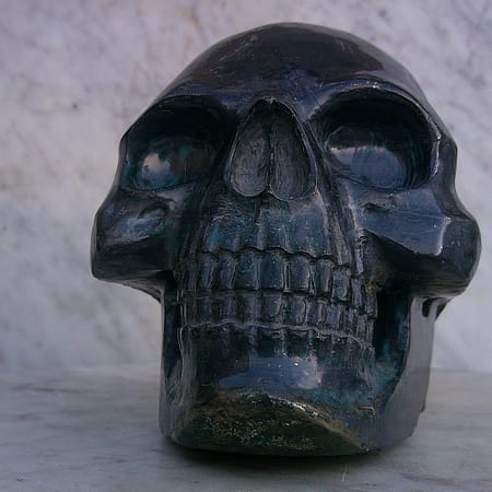 Sculpture de crâne humain en pyrite, vue de face, pièce unique sculptée à la main dans un bloc de minéral naturel, mettant en évidence la symétrie des volumes, les détails anatomiques du visage et les reflets métalliques caractéristiques de la pyrite travaillée à l’atelier.